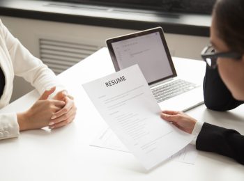 Company CEO and HR manager reading applicant resume or cv while employee waiting for questions, discussion and result during recruitment process in office. Concept of hiring, employment. Close up view